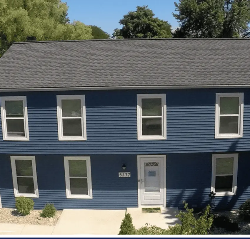 An aerial view of a blue house with a white roof showing exterior **improvement**.