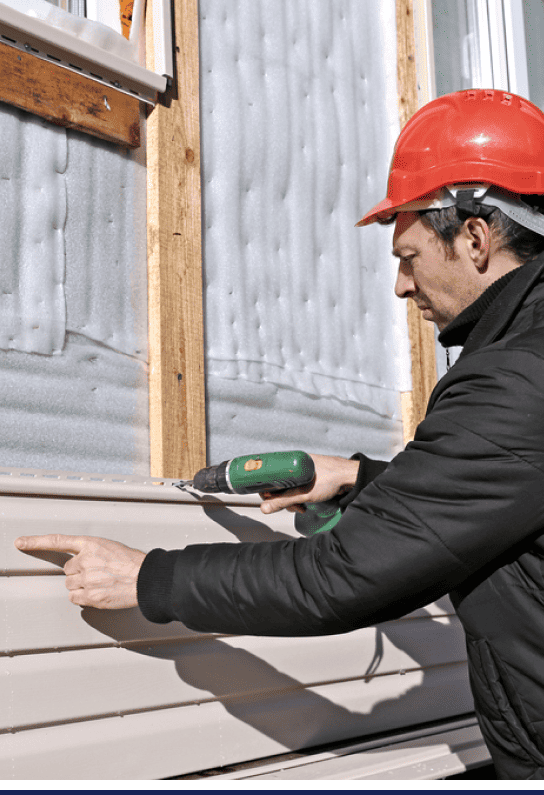 A man is using a drill to install siding on a residential house.