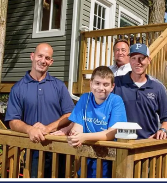 Four men standing in front of an exterior **home** with a boy in a blue shirt.