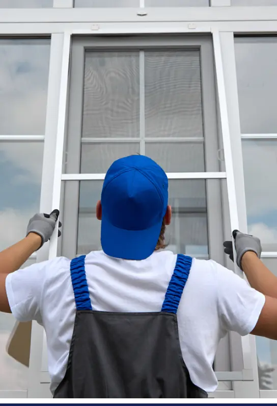 A man wearing blue overalls is working on a window.