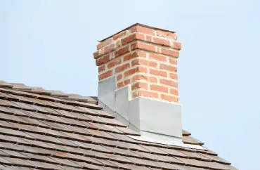 A brick chimney on top of a residential roofing.