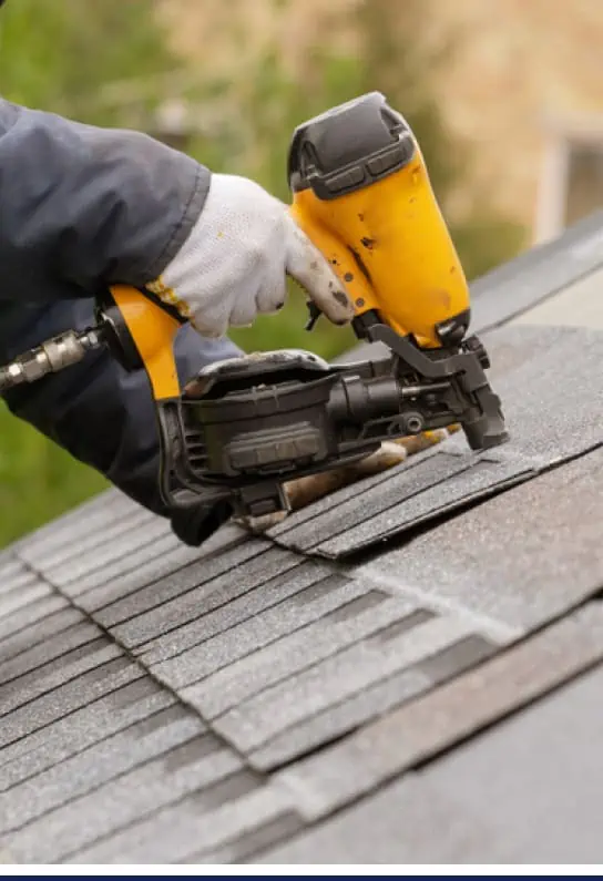 A man using a nail gun on a residential roofing shingled roof.