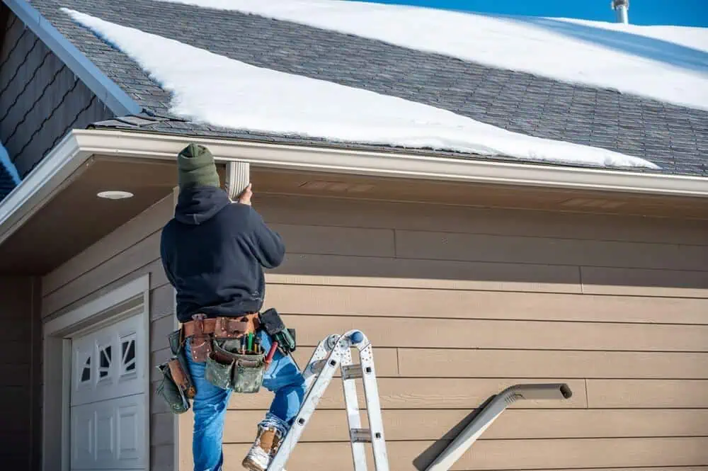 Home improvement contractors on ladder fixing gutters on a snowy roof