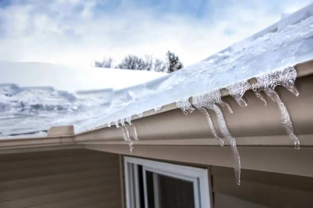 Icicles drip from snowy commercial roof edge under cloudy sky; winterizing essentials.