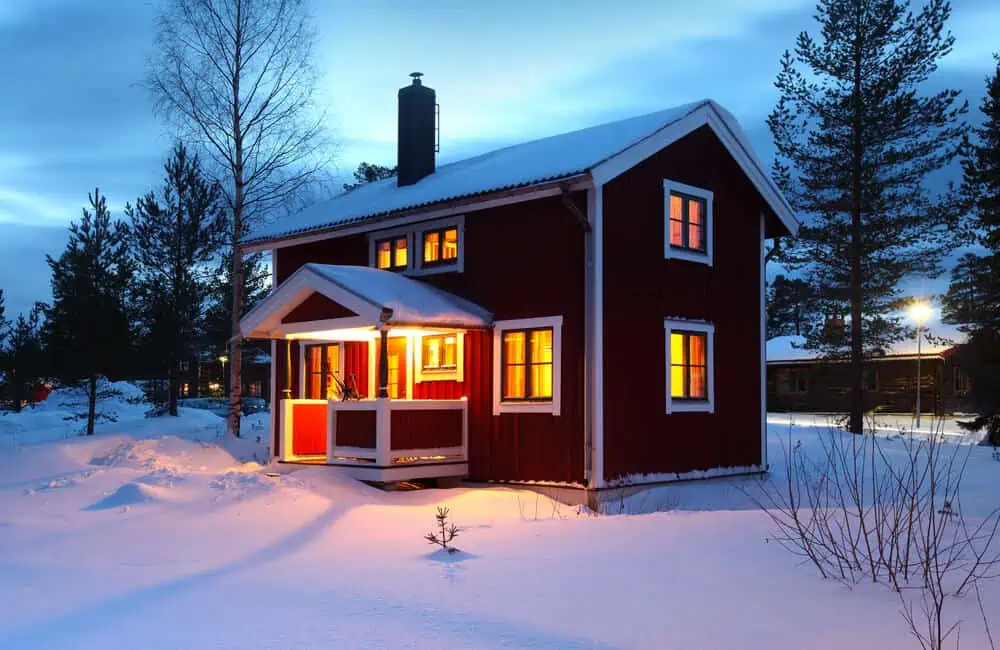 Red house with warm lights, snowy landscape, commercial roof winterization.