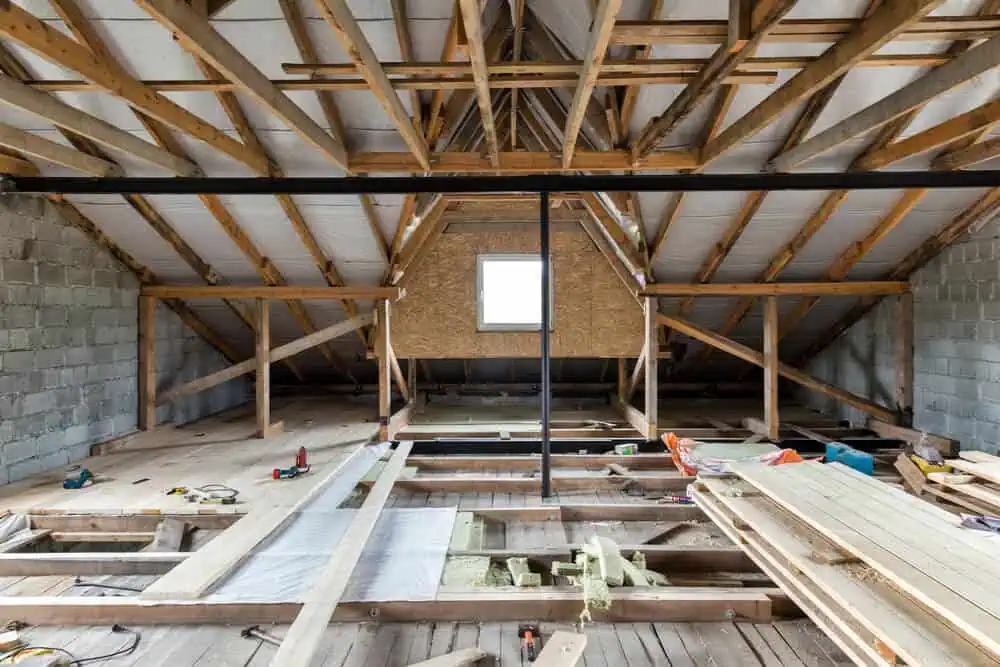 Unfinished attic with exposed beams and roofing materials in renovation process.