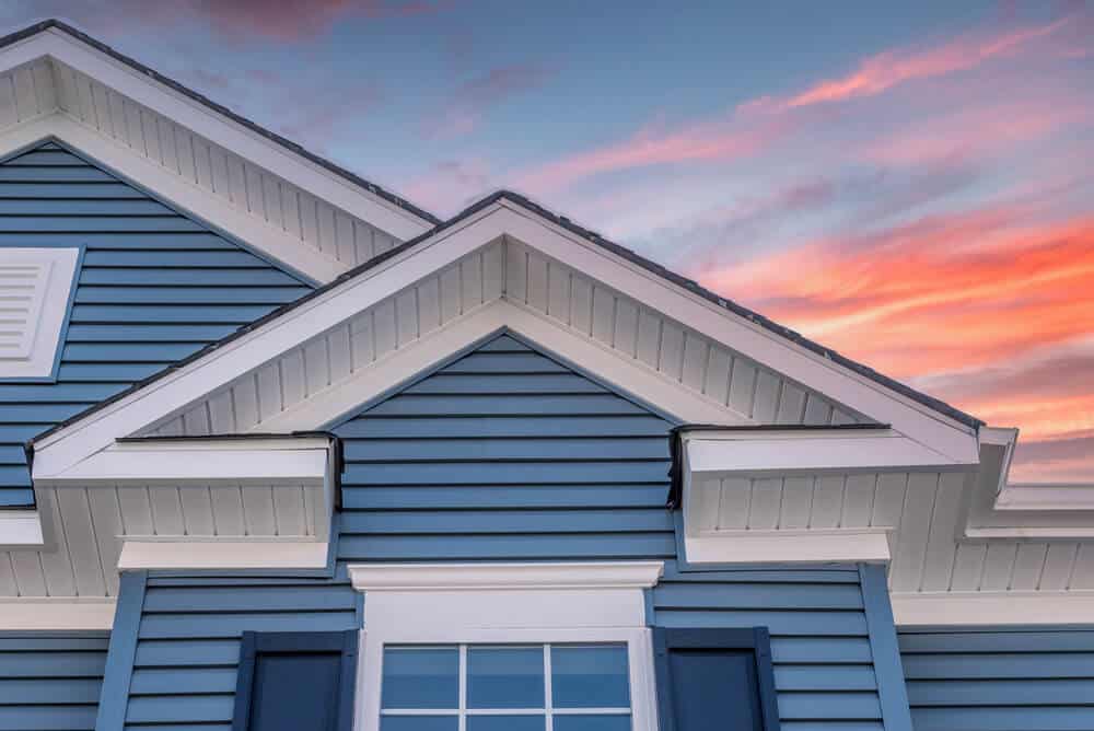 Close up view of gray home with fiber cement siding and trim against a blue and pink sky.