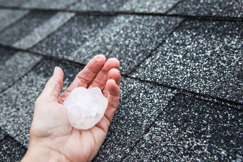 A hand holding a large hail stone against an asphalt roof