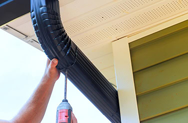 A contractor installs black gutters and downspouts for roofing and gutter services in Michigan.